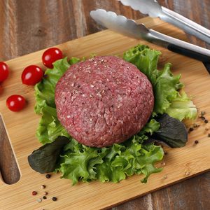 Wagyu ground beef patty on cutting board with lettuce and tomatoes